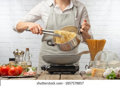 Professional chef in white uniform pours boiled spaghetti in pan for cooking pasta alla carbonara. Backstage of preparing traditional italian dish on white background. Cooking process. Frozen motion.