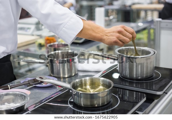 Professional chef workplace at cuisine\
of restaurant. Close up view of man hand stirring soup with spoon.\
Cooking, catering, culinary, gastronomy and food\
concept
