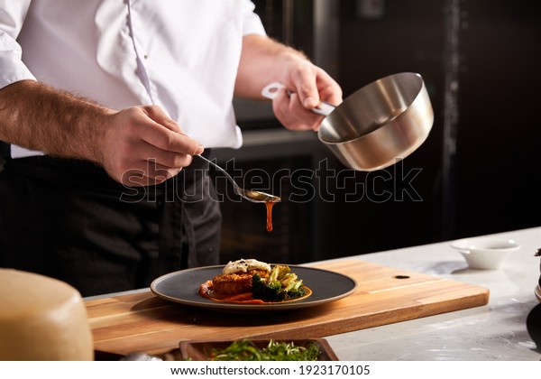 Professional Chef-cook Decorating Dish In\
Restaurant Kitchen Alone. Man In White Apron Makes Finishing Touch\
On DIsh. Culinary, Restaurant, Gourmet\
Concept
