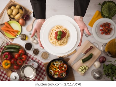 Professional chef's hands cooking pasta on a wooden worktop with vegetables, food ingredients and utensils, top view