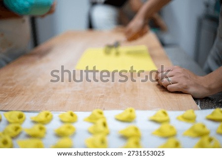 Professional chefs preparing rows of fresh, yellow tortelli pasta by hand, pressing stuffed dough sheets on a floured wooden board, highlighting traditional Italian culinary artistry