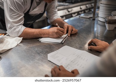 Professional chefs work together in a commercial kitchen, discussing and writing down menu plans. Collaboration, culinary arts, and teamwork are highlighted in this dynamic restaurant environment. - Powered by Shutterstock