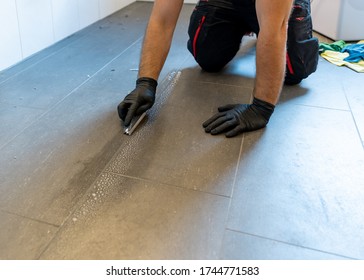 A Professional Cleaner Cleaning Grout With A Brush Blade And Foamy Soap On A Gray Tiled Bathroom Floor