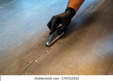 A Professional Cleaner Cleaning Grout With A Brush Blade And Foamy Soap On A Gray Tiled Bathroom Floor