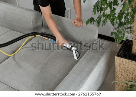 Professional cleaning of fabric sofa using extraction vacuum tool. Ideal for upholstery cleaning service promotion and residential furniture maintenance marketing.