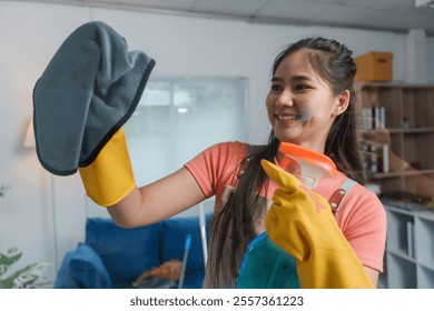 Professional cleaning lady wearing gloves and apron, cleaning a window with microfiber cloth and spray bottle in a modern apartment - Powered by Shutterstock