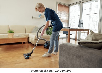 Professional Cleaning lady wearing uniform vacuums floor in living room