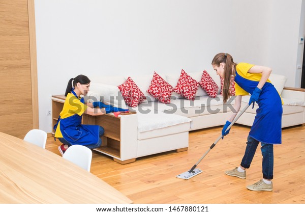professional cleaning service. Two women in working\
uniform, in aprons, divide the cleaning of the kitchen of a private\
house, cottage. Washing\
floor
