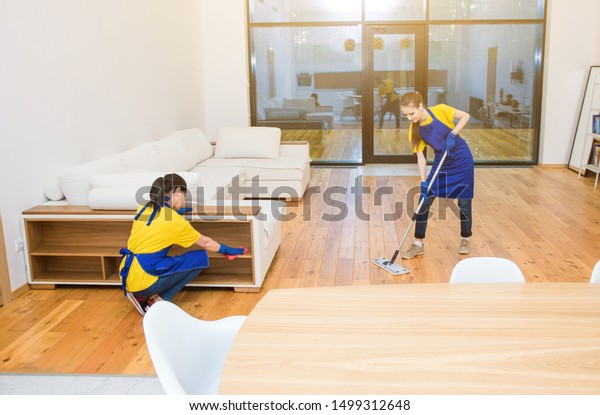 professional cleaning service. Two women in working\
uniform, in aprons, divide the cleaning of the kitchen of a private\
house, cottage. Washing\
floor