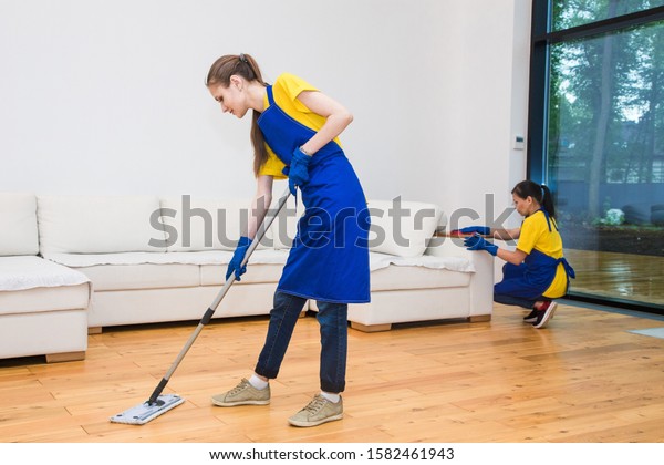 professional cleaning service. Two women in working
uniform, in aprons, divide the cleaning of the kitchen of a private
house, cottage. Washing
floor