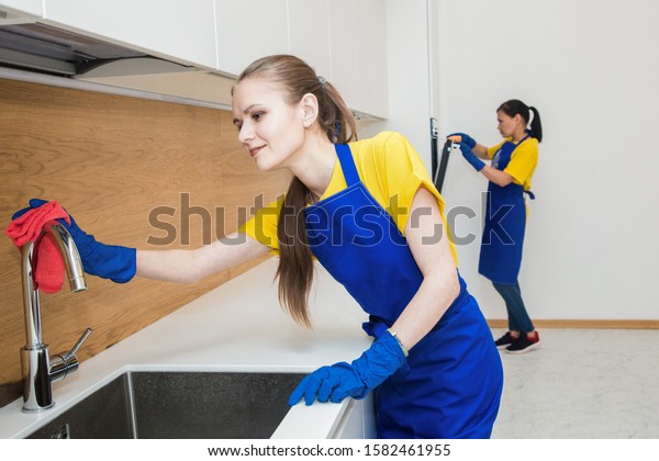 professional\
cleaning service. Two women in working uniform, in aprons, divide\
the cleaning of the kitchen of a private house, cottage. washing\
the refrigerator, tap, sink. Wash\
floor.