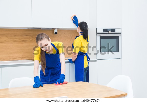 professional\
cleaning service. Two women in working uniform, in aprons, divide\
the cleaning of the kitchen of a private house, cottage. washing\
the refrigerator, tap, sink. Wash\
floor.
