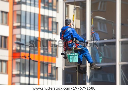 Professional climber rope access worker cleaning the windows on the high rise building, industrial mountaineers washing the glass facade of a modern building, working at heights 