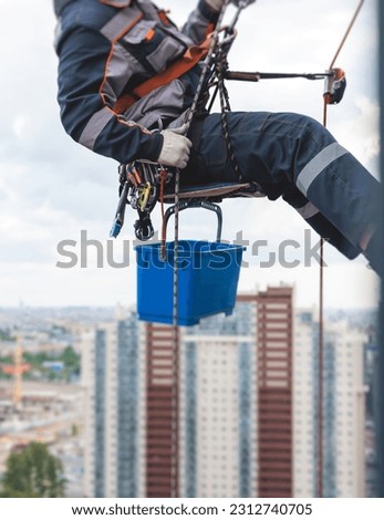 Professional climber rope access worker painting, repairing and cleaning windows on the facade of residential skyscraper high rise building exterior wall, industrial mountaineers working at heights