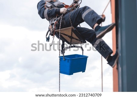 Professional climber rope access worker painting, repairing and cleaning windows on the facade of residential skyscraper high rise building exterior wall, industrial mountaineers working at heights
