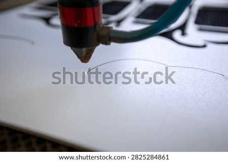 Professional cnc laser cutting machine engraving intricate designs on white material with precision beam focused on surface while metallic nozzle head moves across sheet in industrial workshop