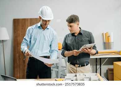 Professional collaboration in architecture. Two engineers work on construction plans, using tools like laptops, tablets, and scale models. Perfect for depicting teamwork  - Powered by Shutterstock