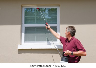 A Professional Commercial Pest Control Service Provider Man Or Do-it-yourself Home Owner Spraying Pesticide On The Outside Of The House To Keep Bugs And Pests Out.