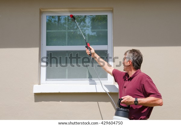 A professional
commercial pest control service provider man or do-it-yourself home
owner spraying pesticide on the outside of the house to keep bugs
and pests out.