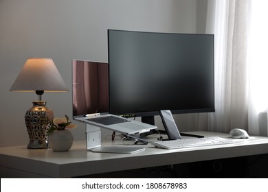 professional computer workstation consisting of a laptop and a large curved monitor on a white desk