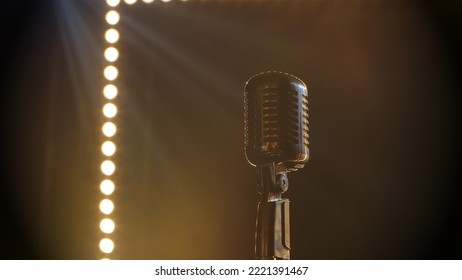 Professional Concert Vintage Glare Microphone. Mic For Record Or Speak To Audience On Stage In Empty Retro Club Close Up. Shot Against A Smoky Background With Yellow Spotlights And Studio Lights Beams