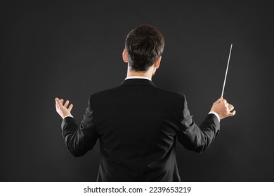Professional conductor with baton on black background, back view