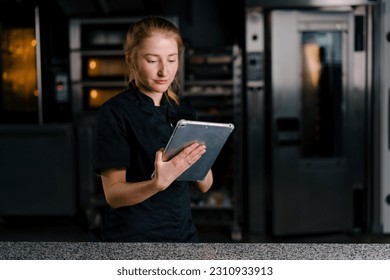 a professional confectioner in a uniform with a tablet in his hands checks the tasks before starting work in professional kitchen - Powered by Shutterstock