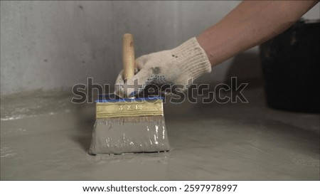 Professional construction worker applying liquid waterproofing membrane on concrete floor using specialized brush for basement renovation and protection