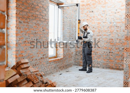 Professional construction worker installing a new window in unfinished brick wall room during home renovation