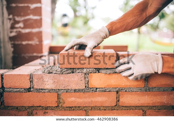 professional construction worker laying bricks and\
building barbecue in industrial site. Detail of hand adjusting\
bricks