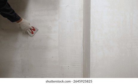 Professional construction worker skillfully smoothing wet plaster on interior wall, carefully leveling surface using specialized putty knife during renovation process