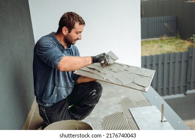 Professional construction worker, tiler laying adhesive and placing ceramic tiles on balcony floor. Details of home renovation, construction works