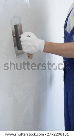 Professional construction worker is using a finishing trowel to carefully apply plaster on a wall, demonstrating expertise in home renovation and interior finishing, close-up of hand