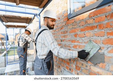 Professional construction workers applying mortar to brick wall, building new house. Craftsmanship and hard work on a construction site