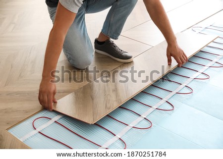 Professional contractor installing underfloor trace heating system indoors, closeup