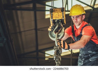 Professional Contractor Lowering the Load Using Large Lifting Hook of Overhead Crane. Indoor Construction Site in the Background. Industrial Theme.