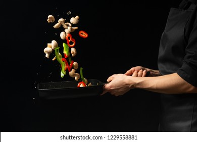 Professional cook. The chef prepares a dish with vegetables and mushrooms in a saucepan. on a black background. menu, recipe book, healthy food, restaurant business