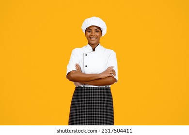 Professional Cook. Smiling Black Chef Woman Posing With Crossed Hands Over Yellow Studio Background, Confident Young African American Cooker Lady In Uniform Looking At Camera, Copy Space - Powered by Shutterstock