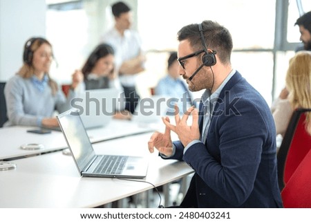 Professional customer support agent counting on his fingers while assisting customers at a call center office, with colleagues in the background.