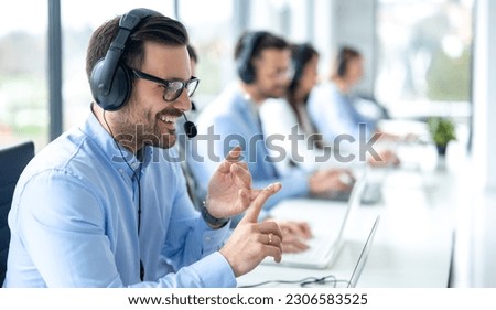 Professional customer support agent man counting on fingers while assisting customers at call center office, with colleagues in the background.