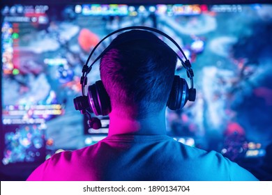 Professional cyber gamer studio room with personal computer for stream in neon color blur background. Back view soft focus.