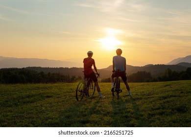 Professional cyclist couple taking a break on a green meadow and watching amazing mountain sunset, aerial shot. - Powered by Shutterstock