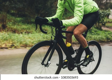 Professional cyclist riding bike outdoors. Male athlete in cycling gear practising on wet road. Cropped shot. - Powered by Shutterstock