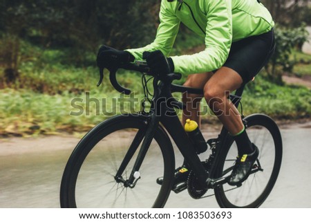 Professional cyclist riding bike outdoors. Male athlete in cycling gear practising on wet road. Cropped shot.