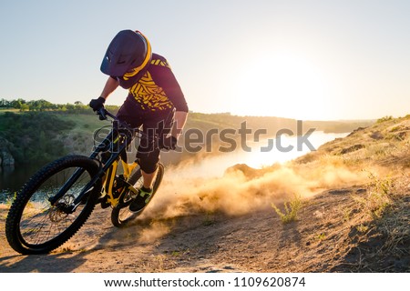 Professional Cyclist Riding the Downhill Mountain Bike on the Summer Rocky Trail at the Evening. Extreme Sport and Enduro Cycling Concept.