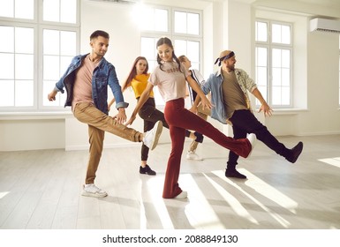 Professional dance crew having fun. Cheerful young people enjoying dance class with coach. Group of happy dancers in trendy casual wear dancing together in sun light in modern dance hall. Lens flare - Powered by Shutterstock