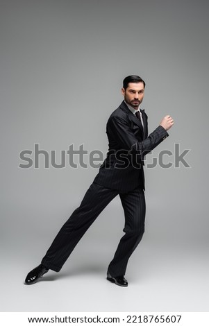Professional dancer in suit performing tango on grey background