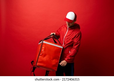 Professional delivery employee man 20s in red cap T-shirt uniform workwear work as dealer courier with red thermal food bag backpack isolated on red background. Service concept. - Powered by Shutterstock