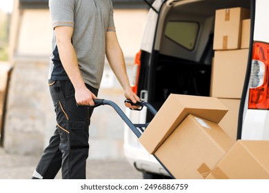 Professional delivery guy pushing a hand truck loaded with packages, express courier and delivery service concept - Powered by Shutterstock