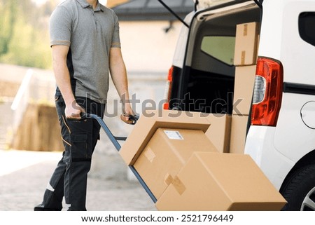 Professional delivery guy pushing a hand truck loaded with packages, express courier and delivery service concept